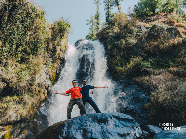 two men standing with their arms out extended holding each other in front of a waterfall