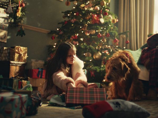 Daisy and her dog Buddy open presents together under a Christmas tree