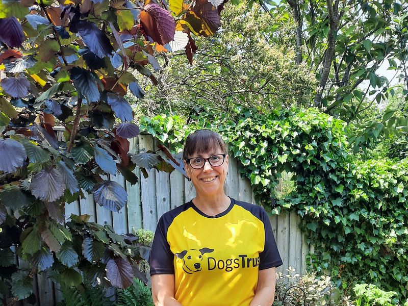 Dog lover Sue in dogs trust yellow and black t-shirt, smiling in a garden. 