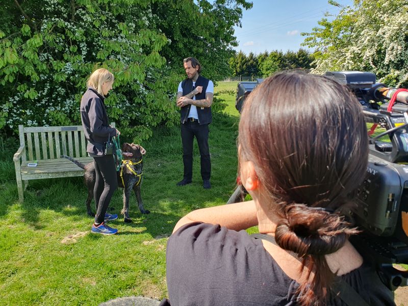 pete standing outside with a member of staff and a brown spotted crossbreed dog. they are being filmed