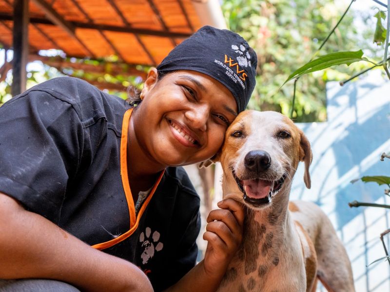 A person wearing a WVS shirt and hat with a dog close to their chest, both appearing happy and relaxed.
